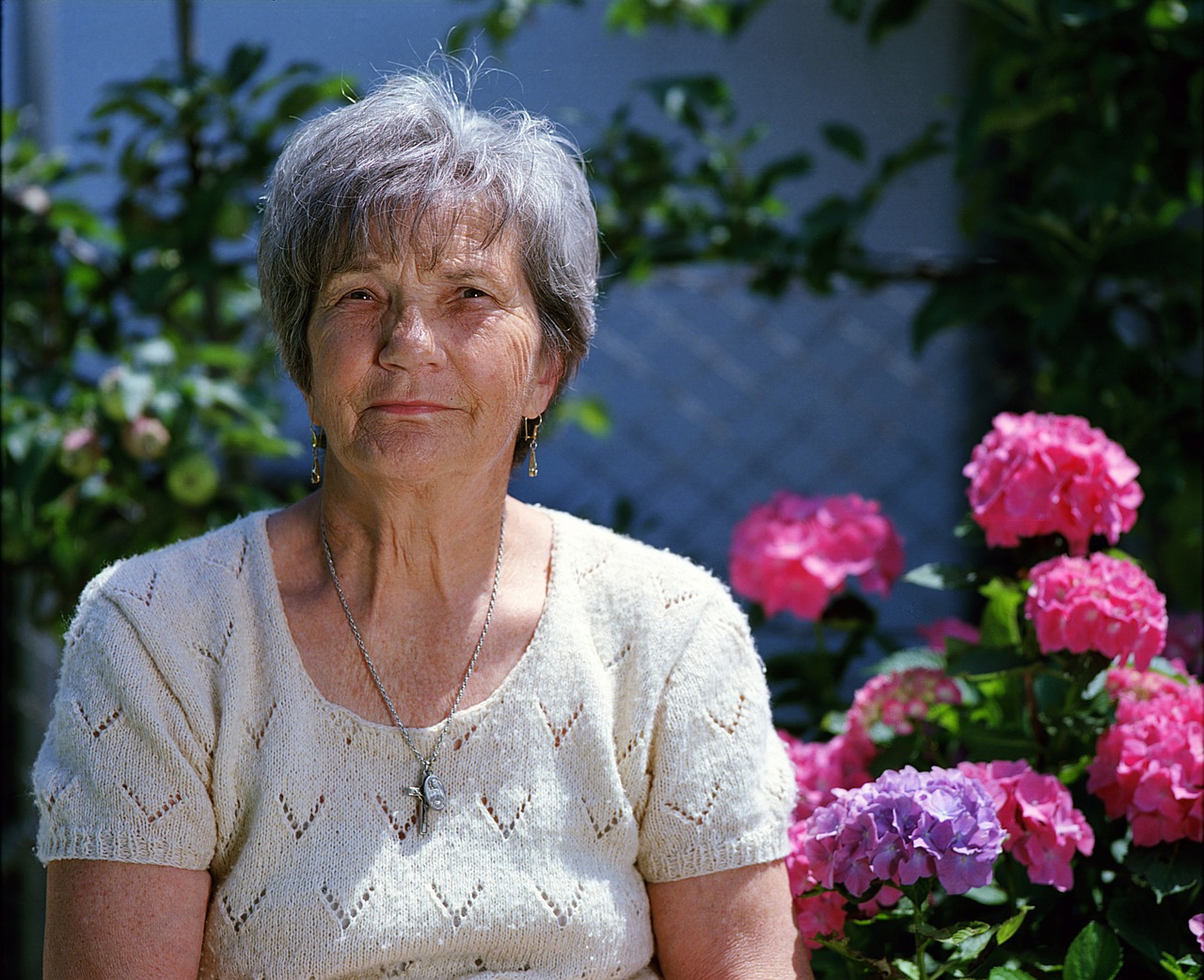 Smiling older woman standing beside pink flowers